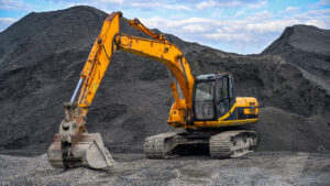 Excavator on gravel site, mountains behind